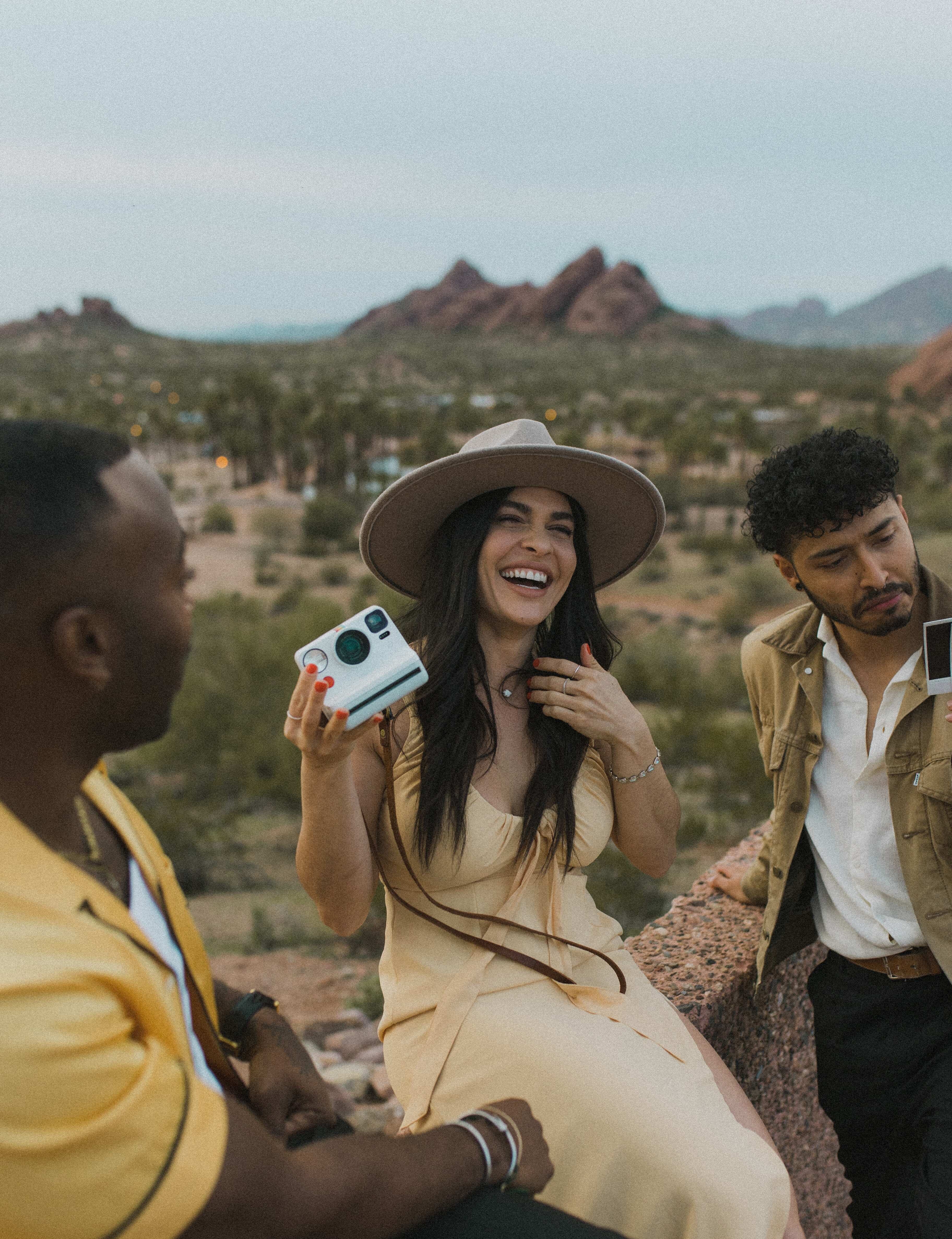 three people laughing with a polaroid camera at papago park in phoenix, arizona